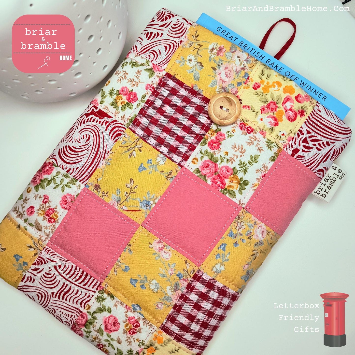 Traditional Book Sleeve in Patchwork Design, Quilted and lined with soft cream coloured calico. The exterior fabric choices are in a range of pinks and yellows, mainly florals with some solid pink and red gingham squares in cotton poplin fabric.