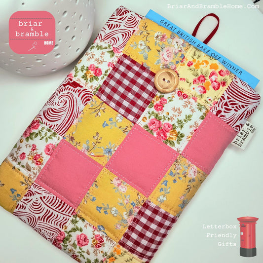 Traditional Book Sleeve in Patchwork Design, Quilted and lined with soft cream coloured calico. The exterior fabric choices are in a range of pinks and yellows, mainly florals with some solid pink and red gingham squares in cotton poplin fabric.
